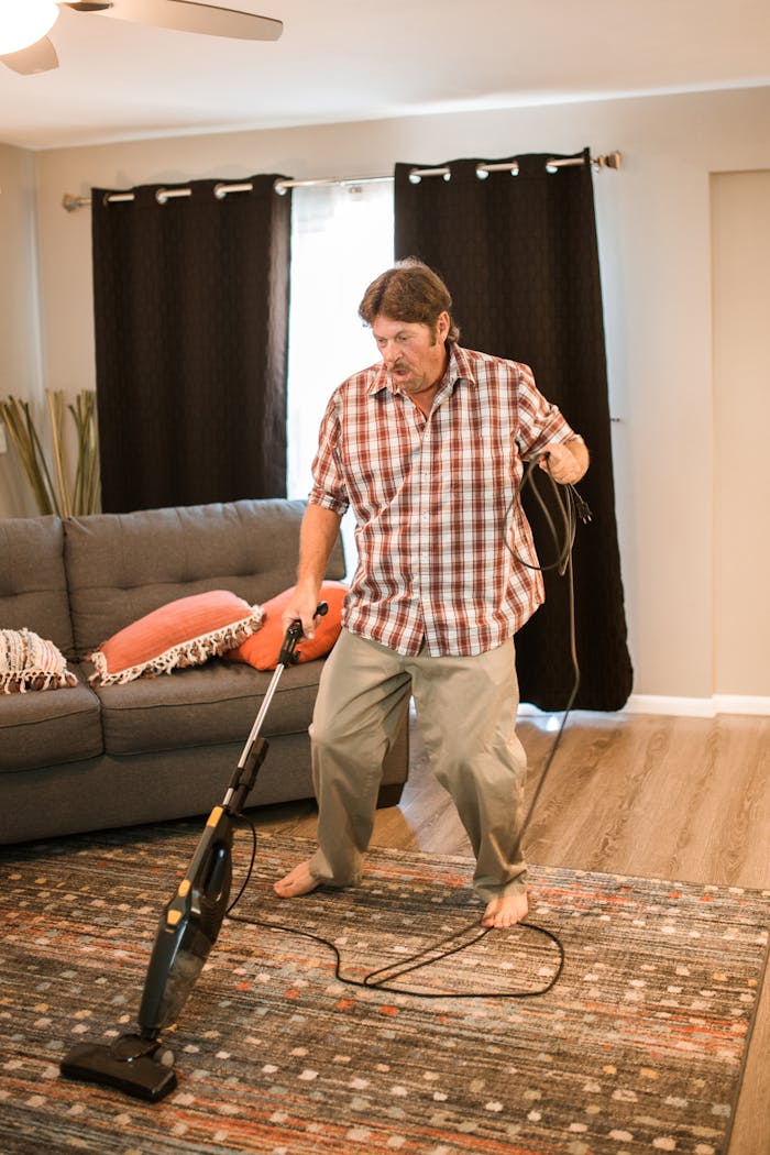 Adult man cleaning carpet with vacuum in cozy living room, demonstrating a home chore routine.